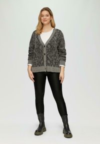 Grijze en zwarte gebreide cardigan met een V-hals, knopen aan de voorzijde en geribbelde manchetten, gedragen over een wit topje en gecombineerd met zwarte faux leren broek en laarzen.