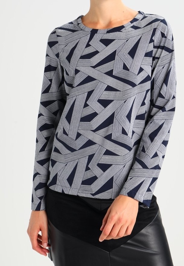 Haut à manches longues avec motif géométrique bleu marine et blanc, porté avec une jupe noire, montrant le haut du corps et les détails des mains.