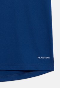 Camisa atlética azul marinho com tecido sintético suave. Apresenta um logotipo "FLASHDRY" impresso em branco perto da bainha. Costuras planas visíveis.