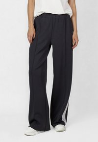 Black athletic pants with a relaxed fit, featuring an elastic waistband and contrasting white side panels. Made of soft, stretchable fabric.