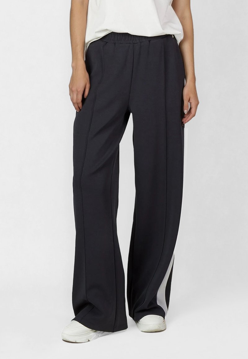 Black athletic pants with a relaxed fit, featuring an elastic waistband and contrasting white side panels. Made of soft, stretchable fabric.