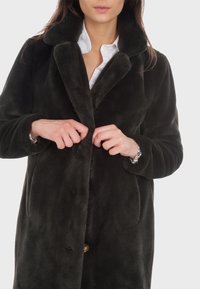 Svart pälsjacka med en stor krage, knappstängning och sidofickor. Materialet verkar mjukt och plyschigt, med en slät yta.