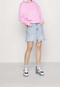 Sudadera rosa con capucha y corte holgado, combinada con una falda vaquera azul claro con dobladillo sin rematar y abertura frontal. Se lleva con zapatillas multicolores.