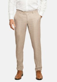 Pantalones de lino beige con un ajuste entallado, con frente plano, pasadores para cinturón y bolsillos. Combinados con zapatos marrones de cordones.