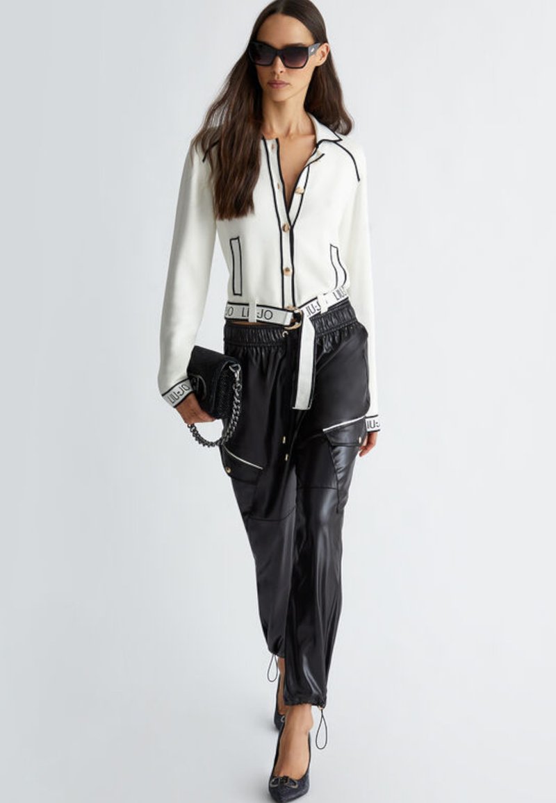Hvid cardigan med sort pipedetalje og guldknapper, sorte faux læderbukser med lommer og en sort clutch med kædeaccent. Solbriller inkluderet.