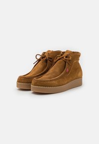 Stivaletti alla caviglia in suede beige con punta tonda, chiusura con lacci, dettagli di cucitura visibile e suola in gomma testurizzata.