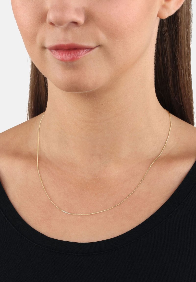 Guldhalsband med en tunn, slät design, som har en rundad form som vilar mjukt på nyckelbenet. Bärs med en enkel svart topp.