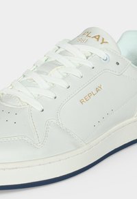Λευκό δερμάτινο αθλητικό παπούτσι με λευκά κορδόνια, μπλε περίγραμμα στη σόλα και χρυσό λογότυπο "REPLAY 1981" στη γλώσσα και την πλευρά.