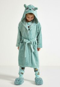 Turkos plyschbadrock med en huva som har djuröron, knytmidja och två framfickor. I kombination med mönstrade pyjamasbyxor och fluffiga tofflor.