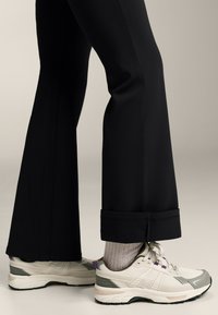 Black flared pants with a cuffed hem paired with beige running shoes. The shoes feature light gray accents and a textured sole.