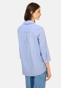Camicia a righe blu e bianche con colletto, maniche a tre quarti e dettaglio del giromanica nella parte posteriore. Vestibilità morbida con una texture delicata.