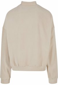Beige fleece genser med høy krage, senkede skuldre og ribbestrikkede mansjetter. Myk tekstur og avslappet passform, med kortet lengde.