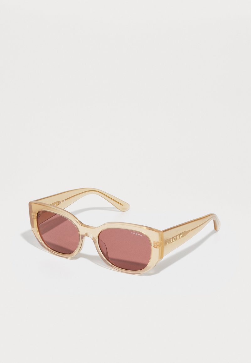 Ochelari de soare din plastic de un chihlimbar deschis, cu rame pătrate și lentile roșii închise. Logo-ul „Vogue” fiind embosat pe brațele ochelarilor. Finisaj neted și lucios.