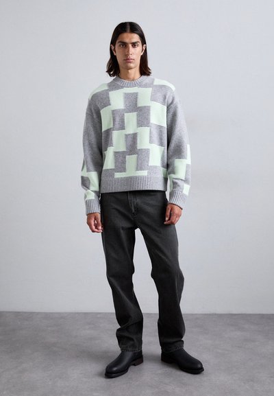 Grijze en mintgroene trui met geometrische patronen, geribde manchetten en zoom. Gecombineerd met donkere jeans en zwarte laarzen, tegen een neutrale achtergrond.