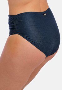 Parte inferior de bikini de cintura alta en azul marino oscuro con una textura brillante, con frunces a los lados y un pequeño logo metálico como detalle.