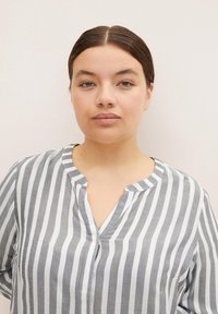 Camisa de rayas verticales grises y blancas con cuello de pliegue, textura suave y corte relajado. Diseño sencillo sin patrones ni acentos adicionales.