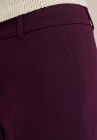 Burgundy trousers featuring a tailored fit, smooth texture, and a front pocket detail, with a sturdy waistband.