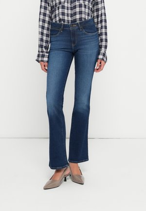 Geflarede blauwe jeans van denim, met een getailleerde taille en voorzakken, gecombineerd met een geruite overhemdresshirt en beige hoge hakken.