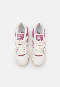 Baskets en cuir blanc avec des accents roses, dotées d'une boîte à orteils perforée, de lacets plats et du logo New Balance sur la languette et le côté.