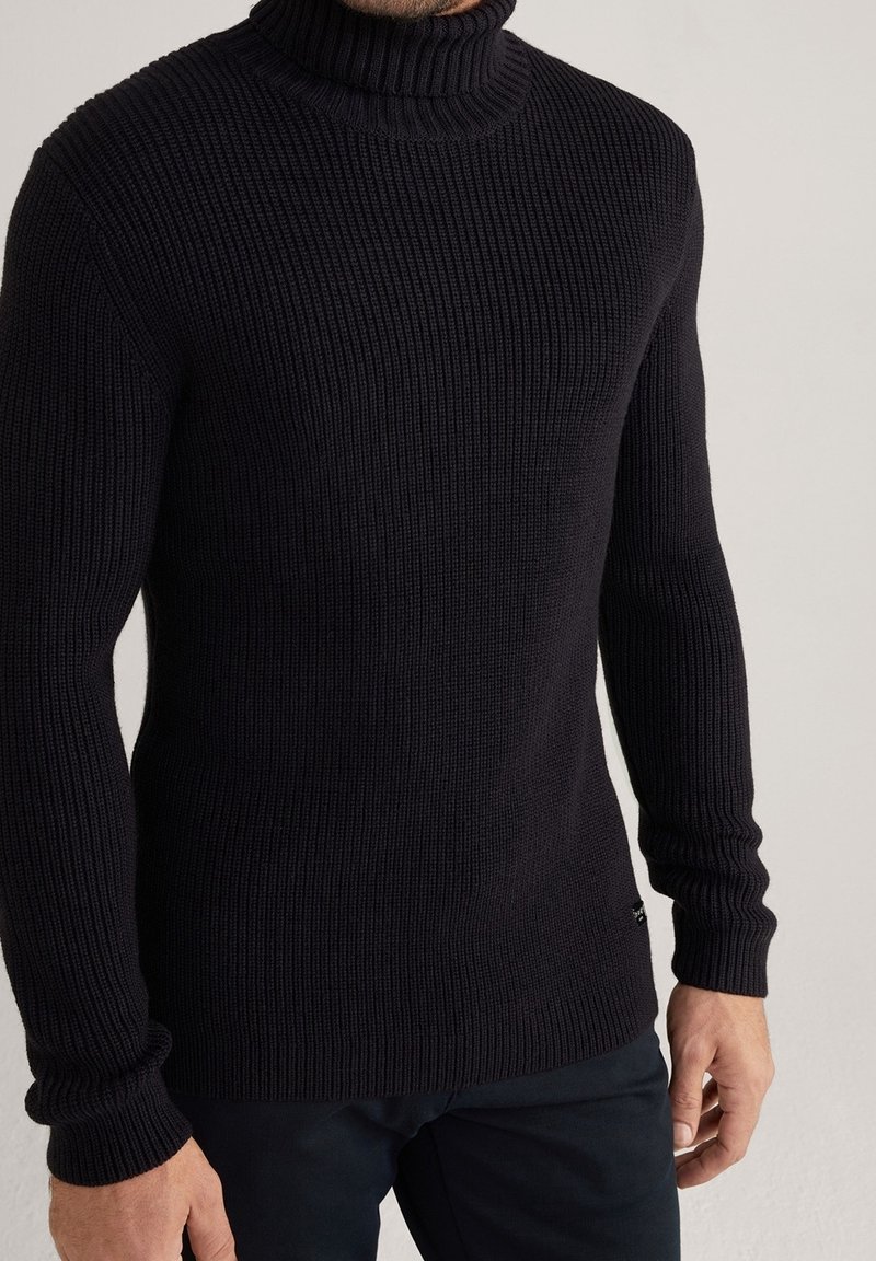 Svart ribbad polotröja i texturerad stickad väv, med långa ärmar och en figurnära design, med en subtil varumärkesdetalj i botten.