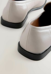 Lichtgrijze leren schoenen met een ronde neus en een zwarte rubberen zool, met een gladde textuur en subtiele stiksels bij de hiel.