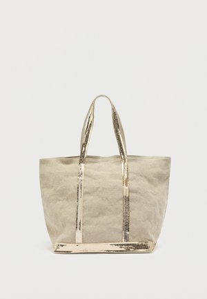 Sac fourre-tout en toile beige avec des anses et une base en métal doré, présentant un design simple et non structuré ainsi qu'une surface légèrement texturée.