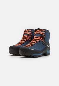 Buty trekkingowe z granatowym zamszowym wierzchem, jaskrawopomarańczowymi sznurówkami, czarną gumową osłoną na palce oraz solidną podeszwą zapewniającą przyczepność. Lekka konstrukcja.
