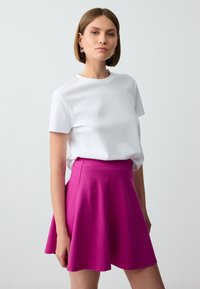 T-shirt bianco in cotone abbinato a una gonnellina fluttuante fucsia che arriva al ginocchio. Il tessuto è liscio, con un semplice scollo tondo e maniche corte.