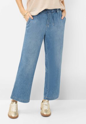 Lyseblå vidde ben jeansbukser med elastisk talje og snøre, båret med guld sneakers og beige top stoppet ind.