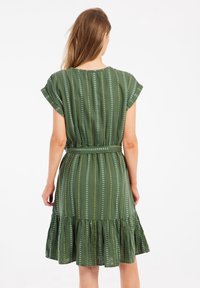 Grünes Kleid mit Cap-Ärmeln, taillierter Taille und Rüschensaum. Es hat vertikale Streifen mit weißen und gelben Akzenten.