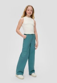 Witte geribbelde mouwloze top met een franjeszoom, gecombineerd met teal wijdvalie cargo broek met zijzakken, gedragen met witte sneakers.