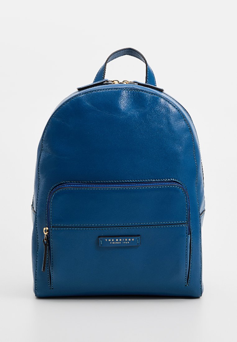 Zaino in pelle blu con forma arrotondata, tasca frontale con zip e logo impresso. Texture liscia con dettagli neri e accessori dorati.