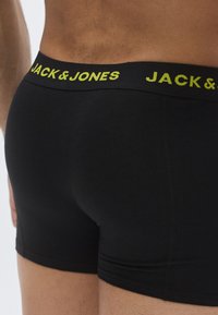 Boxers noirs à coupe ajustée. La ceinture arbore un logo "JACK & JONES" jaune vif. Tissu lisse avec un style minimaliste.