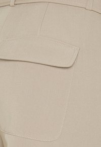 Pantalons beiges avec une poche plaquée à l'arrière, dotés de détails de couture subtils et d'une finition en tissu lisse et texturé.
