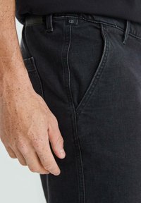 Czarne dżinsy w slim fit, z jedną przednią kieszenią, widocznym przeszyciem oraz oznaczeniem marki na pasku. Teksturowana tkanina.
