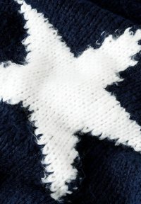 Der gestrickte Wollstoff zeigt ein großes weißes Sternmuster auf einem dunklen Marineblau. Die Textur ist weich und flauschig, mit sichtbaren Nähdetails.