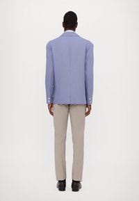 Purple blazer with a structured design, featuring a straight back, notched lapels, and buttoned cuffs, paired with light beige trousers.