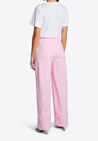 Brede roze broek met een gladde textuur en elastische tailleband, gecombineerd met een eenvoudig wit T-shirt met korte mouwen, gezien vanaf de achterkant.