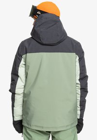 Chaqueta de esquí en tres colores: gris oscuro, verde menta y verde claro. Cuenta con capucha, tejido texturizado y acentos en negro a lo largo de las mangas.
