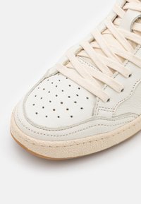Weiße Leder-Sneaker mit perforiertem Zehenbereich, cremefarbenen Schnürsenkeln und einer strukturierten Gummisohle. Verfügt über dezente Nähte und ein körpernahes Design.