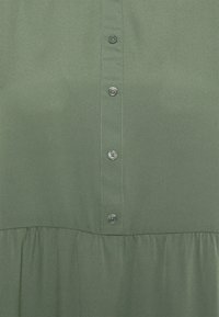 Vestido verde de botões, feito de tecido suave. Apresenta um colarinho, botões frontais e uma bainha de saia plissada.