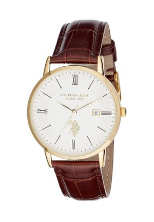 Montre ronde classique en or avec cadran blanc, chiffres romains noirs, guichet date à 3 heures et bracelet en cuir marron à texture crocodile.
