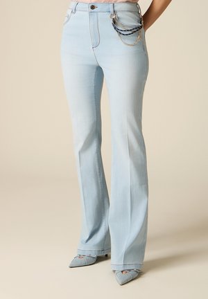 Hellblaue Jeans mit hoher Taille und ausgestellten Beinen, dekorative Kette an der Tasche, kombiniert mit spitzen Pumps aus passendem Denim-Stoff.