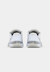 White athletic shoes with a textured upper, padded collar, and a rubber sole. Features a silver logo on the heel and minimalistic design.