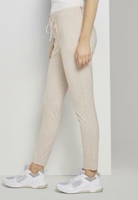 Beige stretchiga joggingbyxor med dragsko i midjan, med smal passform och slät textur, kombinerat med vita sportiga sneakers.