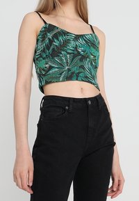 Haut court vert et noir avec un motif feuillu et des bretelles spaghetti fines, associé à un jean noir taille haute.