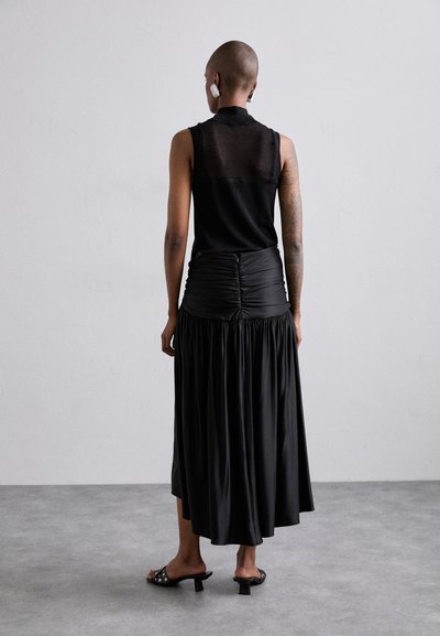Zwarte mouwloze top met doorschijnende details, gecombineerd met een zwarte geraffineerde rok. Gladde stof en een vloeiende silhouet. Chunky hak sandalen.