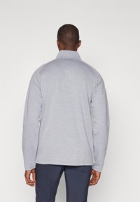 Lys grå genser med krage, lange ermer og rett kant. Stoffet ser mykt ut med en jevn tekstur. Diskret merkevare på nakken.