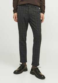 Graue karierte Hose mit taillierter Passform, cropped Länge und Fronttaschen, kombiniert mit schwarzen Schuhen und dunklen Socken.