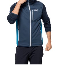 Marinblå softshell-jacka med full dragkedja, kontrasterande turkosa sidopaneler, texturerade ärmar och en ficka på bröstet med dragkedja.